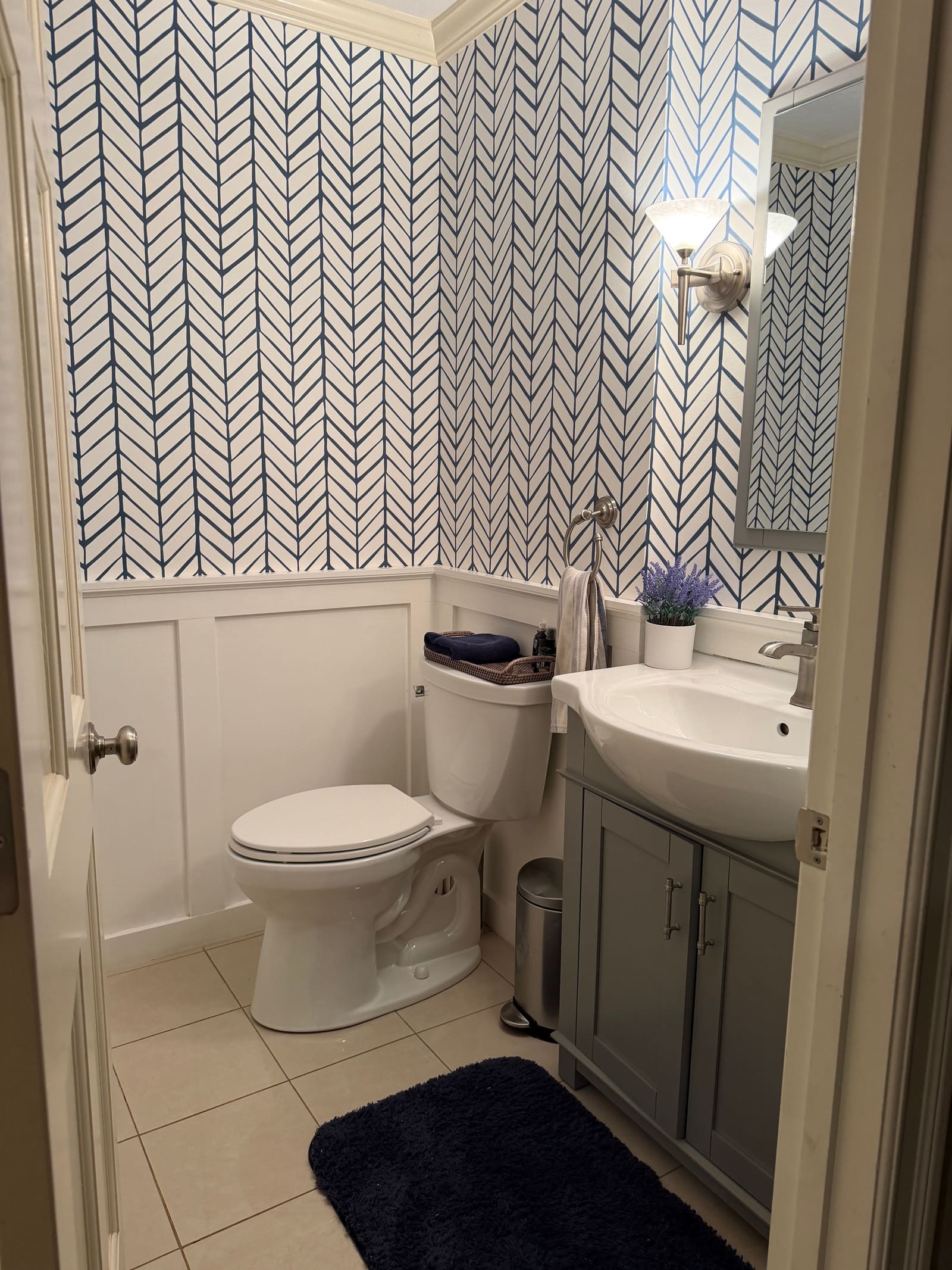 The same powder room after the update, with wainscoting, herringbone wallpaper, a new vanity and fresh trim