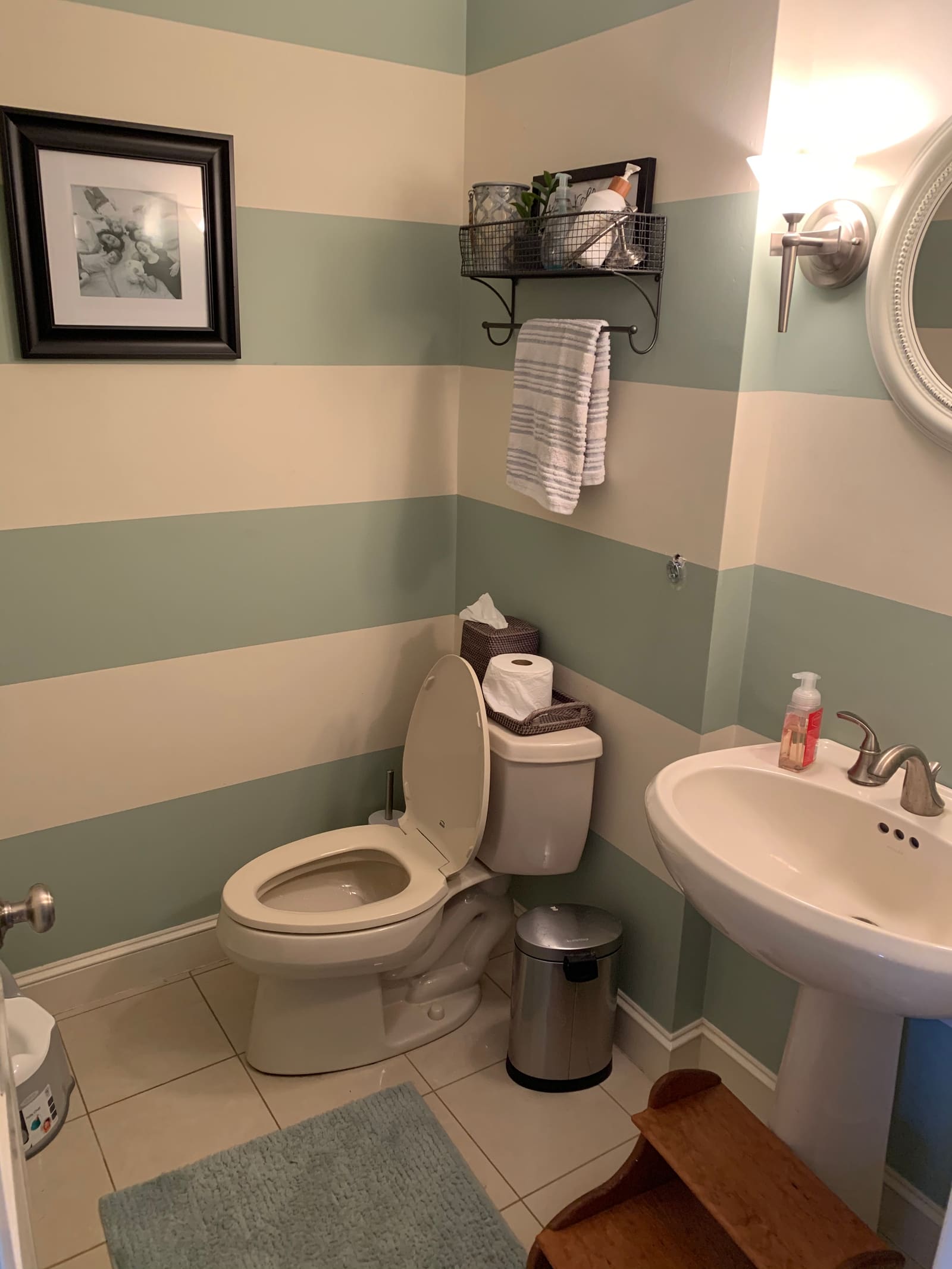 A powder room before the update, with striped painted walls, a pedestal sink and plain trim