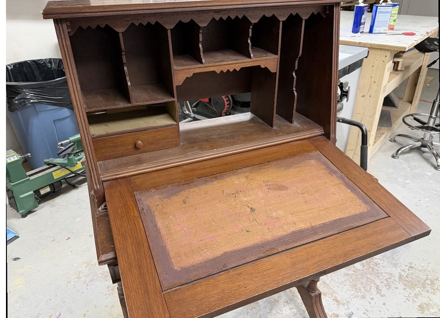 An antique slant-front desk before refinishing, with a worn writing surface and dull wood