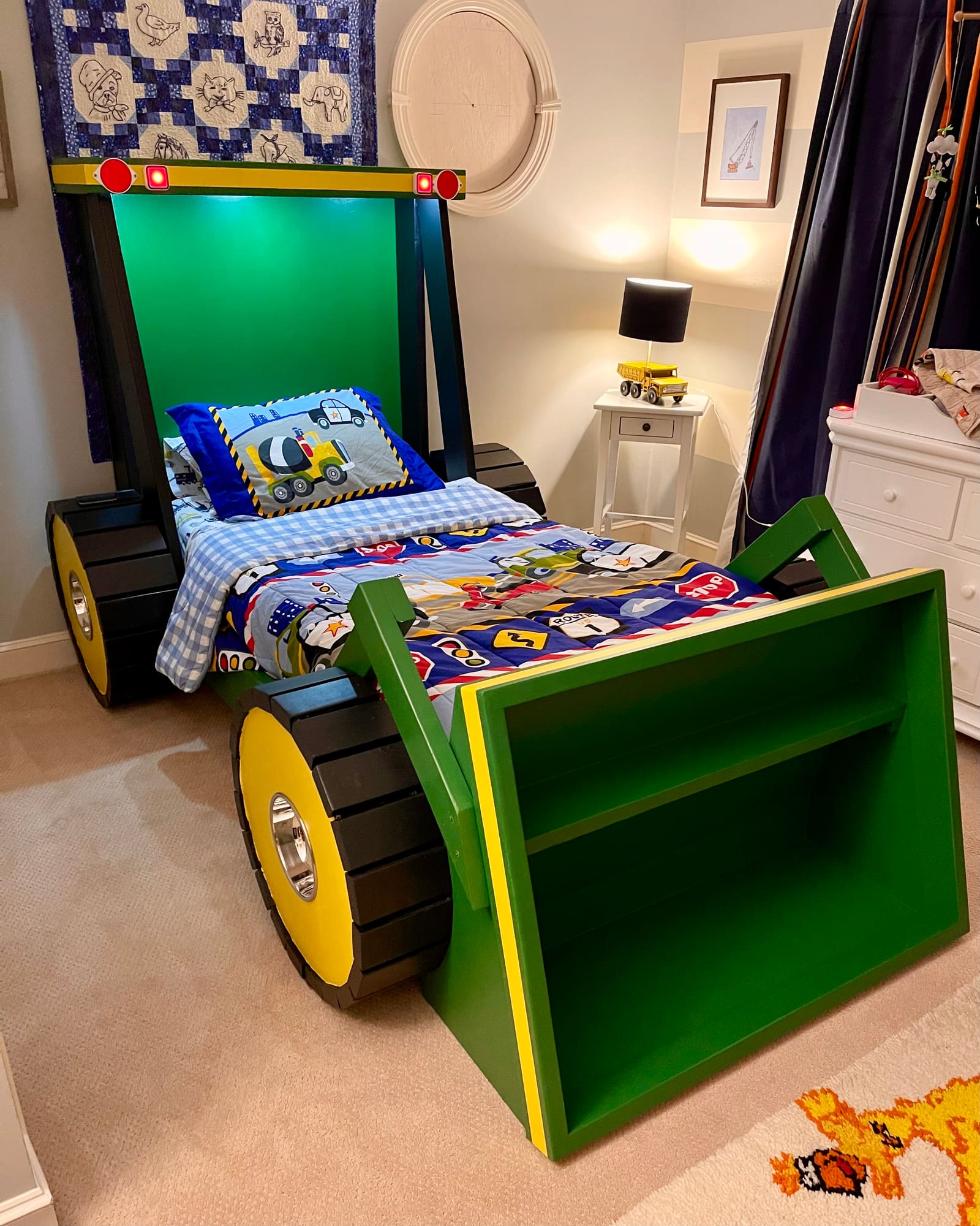 The finished custom tractor bed in a child's room, painted green with yellow wheels and a built-in front loader shelf