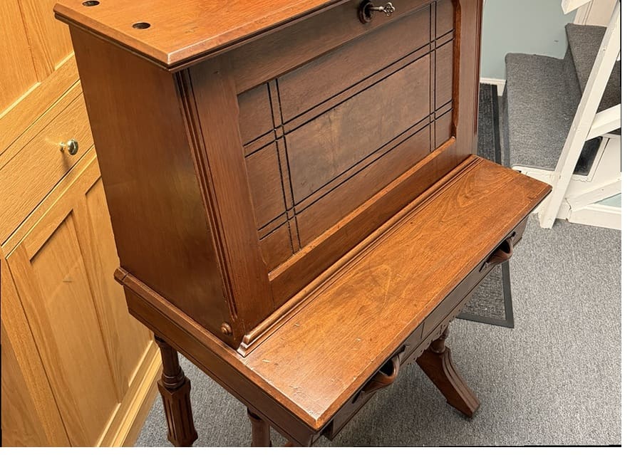The side and legs of the same antique desk after refinishing, with a clean, warm finish