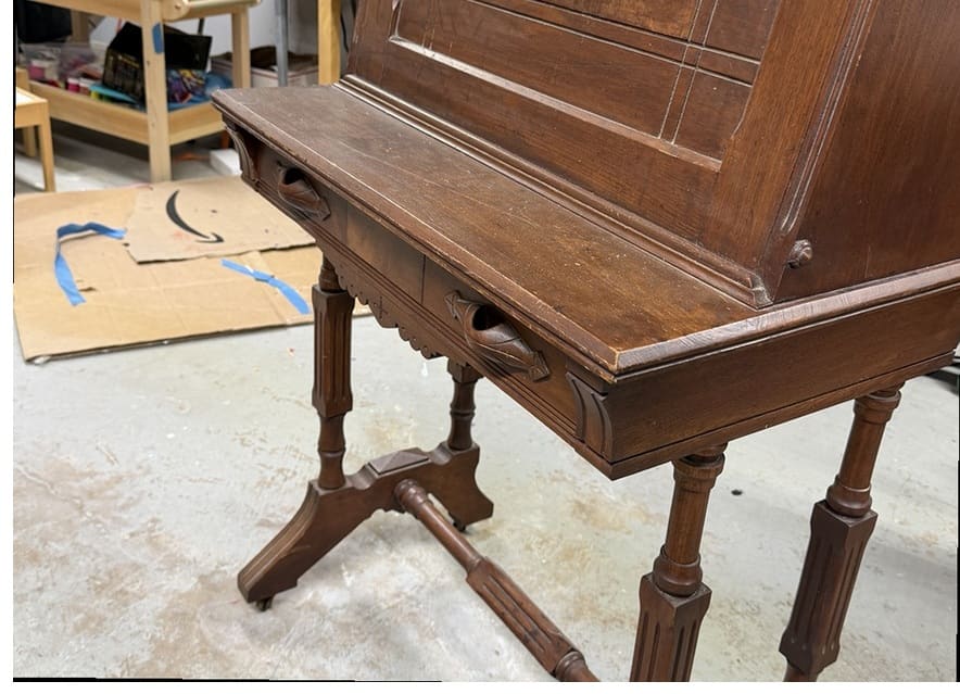 The side and legs of an antique desk before refinishing, with a dark, worn finish