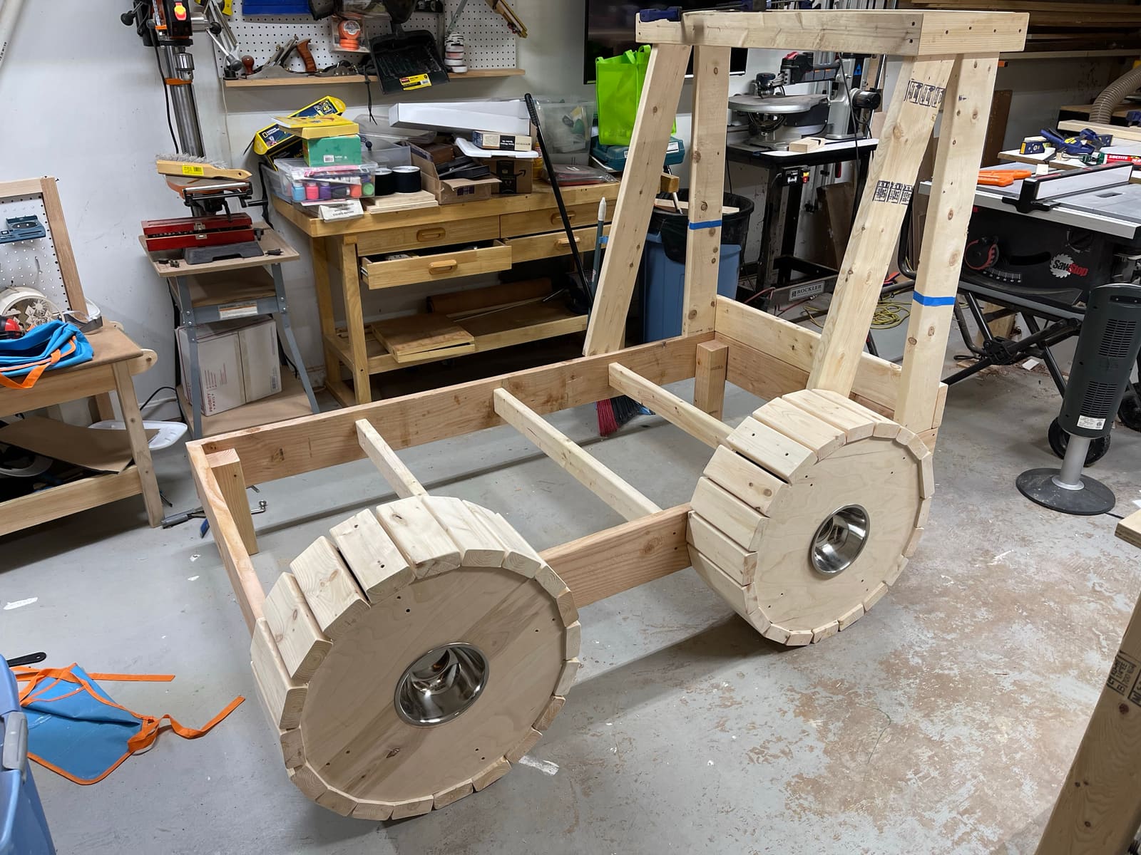 A custom tractor bed frame under construction in the shop, with raw wood and slatted wheels