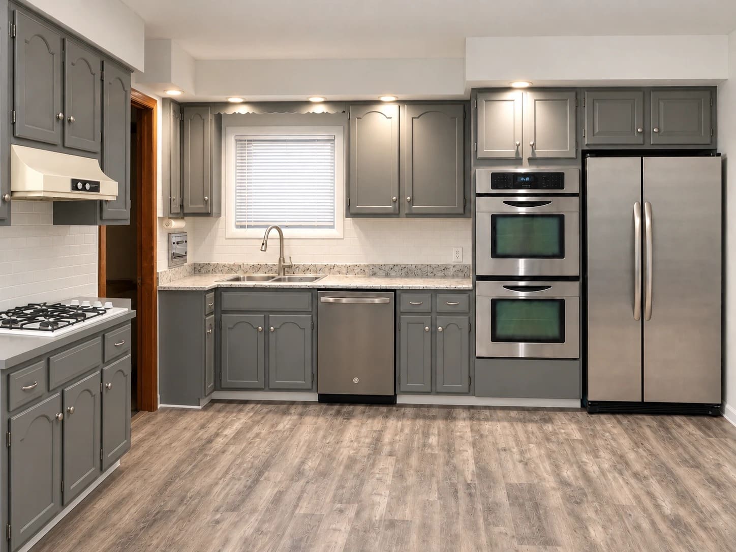 A kitchen with refinished gray cabinets, a granite counter, double wall ovens and wood-look plank flooring