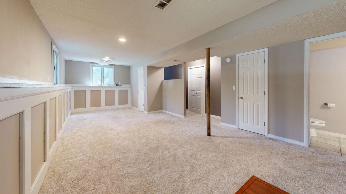 A finished basement room with wainscoting, recessed lights and carpet